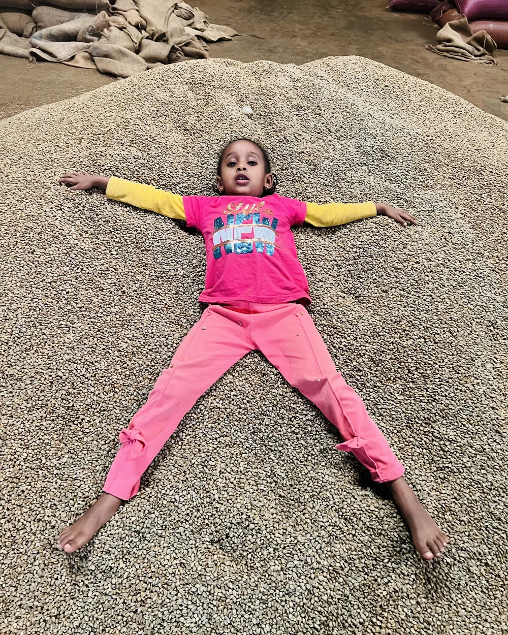 A child lying happily on a mountain of coffee beans